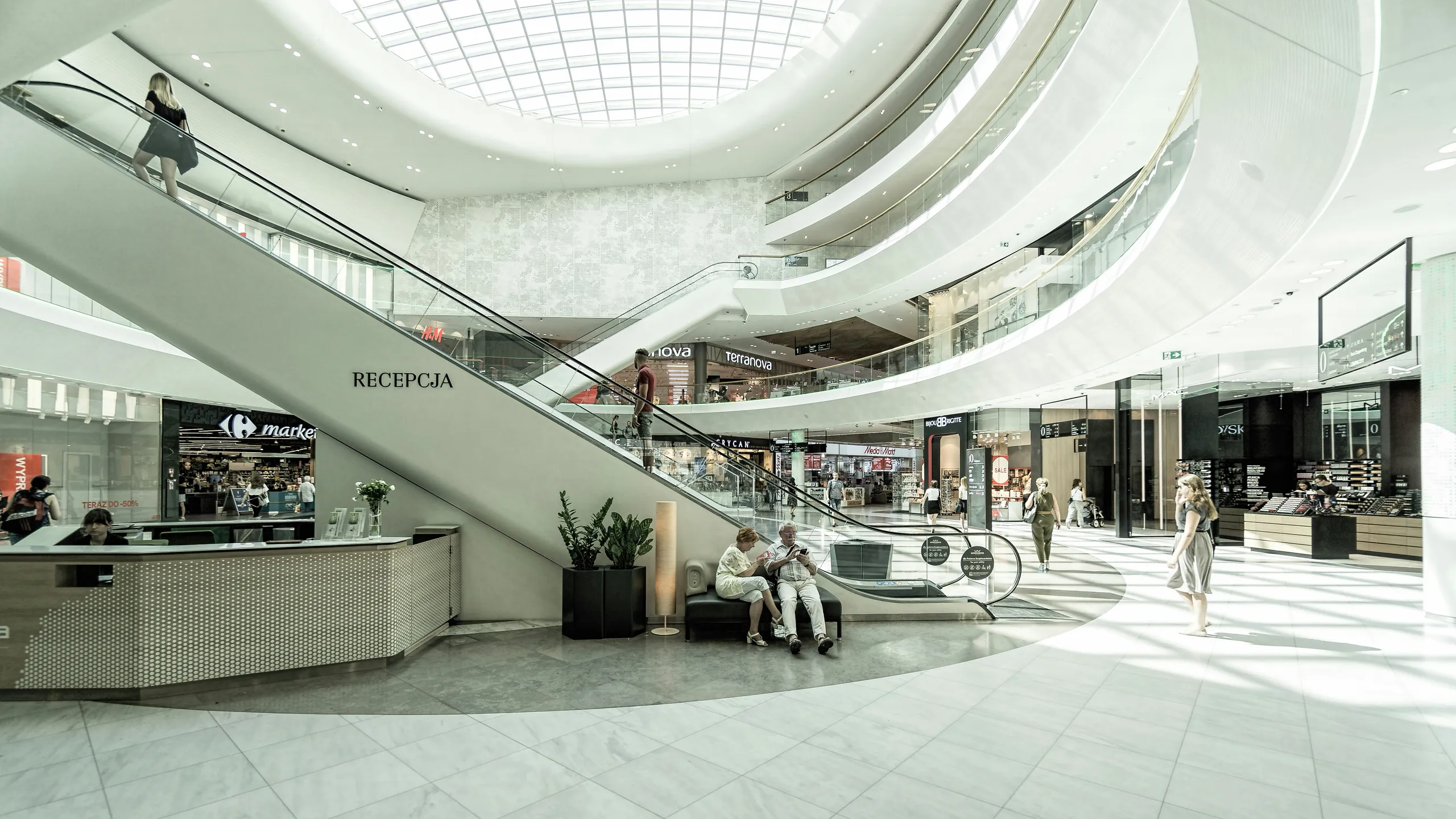 Rozświetlone wnętrze przestronnej hali z galeriami i schodami ruchomymi